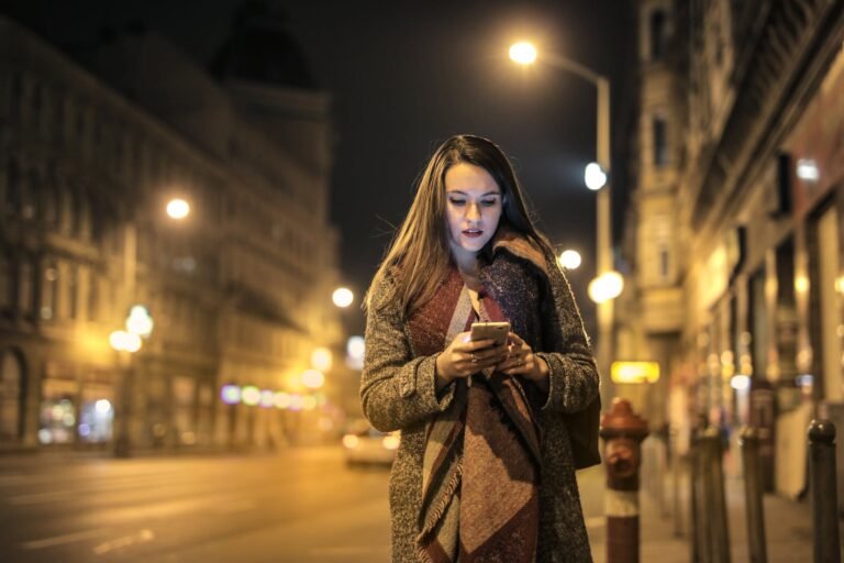 woman walking on sidewalk holding smartphone