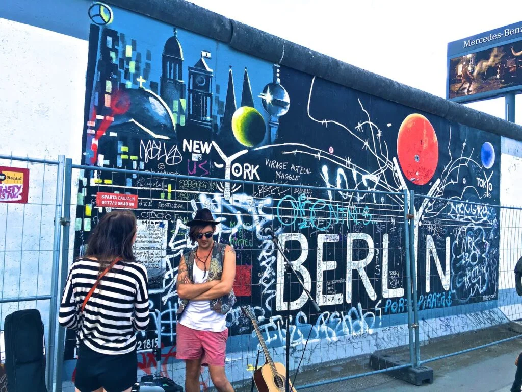 Viaggio in solitaria a Berlino: consigli per godersi il viaggio da soli in totale sicurezza 9 man wearing black waistcoat and white tank tops standing near a mural