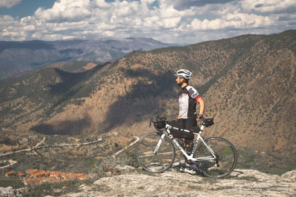 man with his bicycle on top of the mountain under the cloudy sky